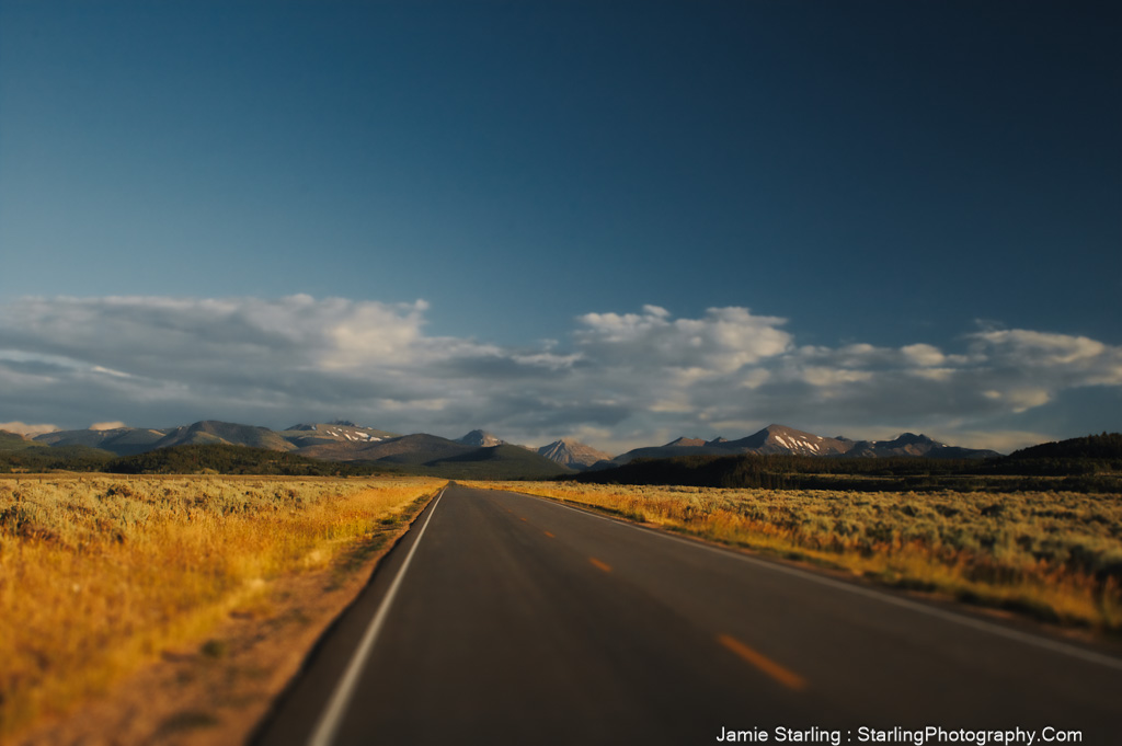 A photograph of an empty road stretching towards a mountain range under the soft, golden light of dawn, symbolizing the journey of awakening and the quest for a deeper understanding of reality.