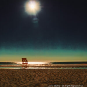 A peaceful beach scene at night with a single empty lifeguard chair, the moon casting a luminous trail over the waves, symbolizing the quiet awakening of the senses and the introspective journey into life’s natural rhythms.