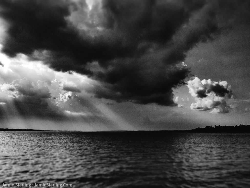 A monochrome seascape where sunlight pierces through stormy clouds, a vivid representation of overcoming life's challenges with resilience and finding hope in moments of darkness.