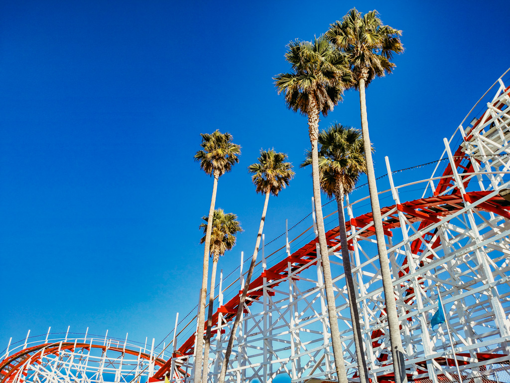 A vibrant image capturing the essence of surrender against life's complexities, with palm trees swaying by a roller coaster, inspiring a journey of acceptance and growth.