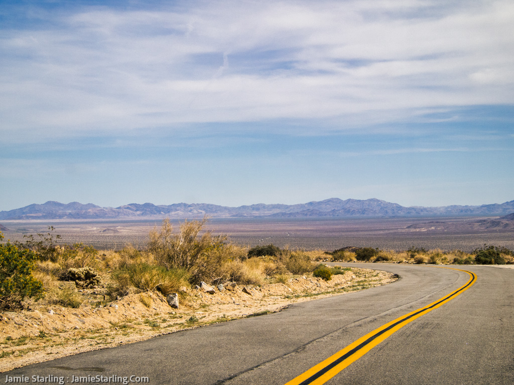 A winding road beckons in the desert, symbolizing the individual's journey towards self-discovery, against a backdrop of distant mountains under a vast sky.