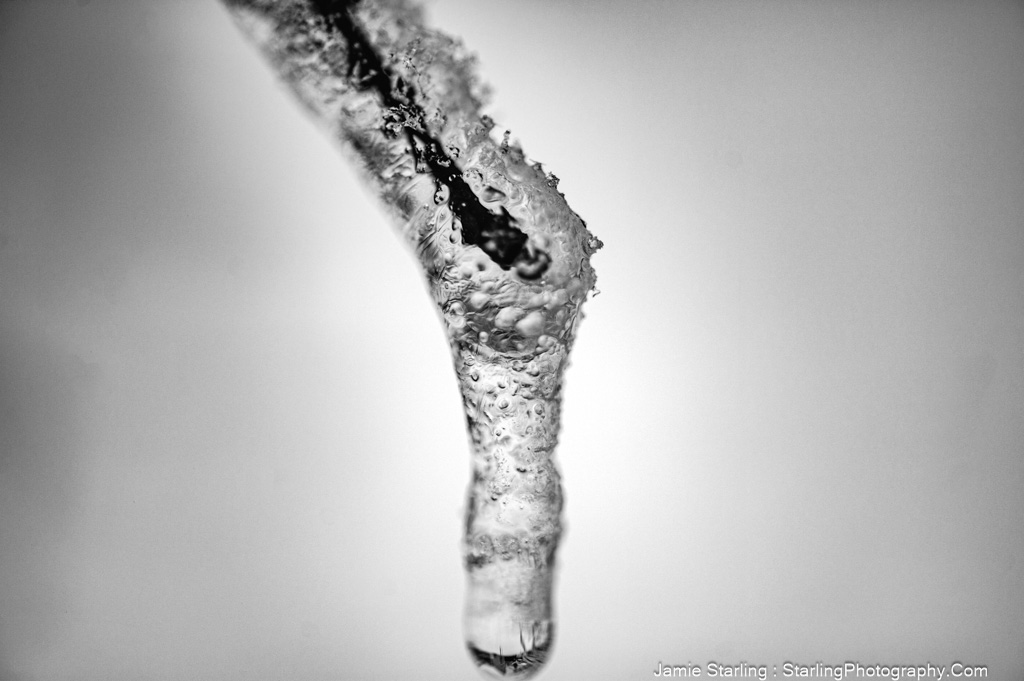 A detailed close-up of a water droplet at the cusp of falling from a frozen icicle, symbolizing a pause in the hustle of life and inviting contemplation.