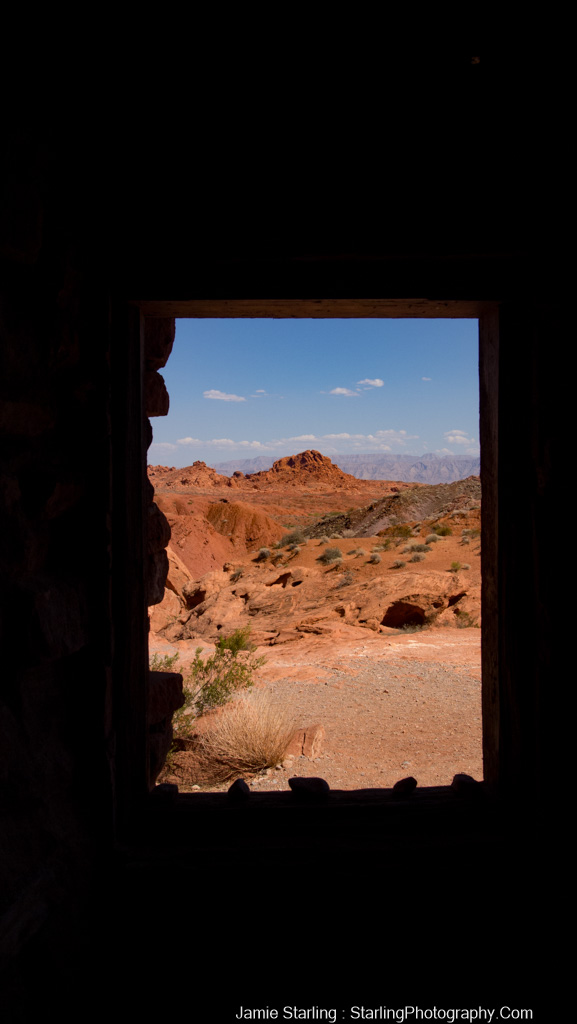 View of a peaceful rocky landscape with bright sunlight and deep shadows seen through an old wooden window, symbolizing serenity and balance in life.