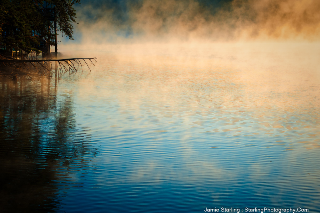 A serene dawn scene where a misty, motionless lake offers a moment of peace, beckoning viewers to slow down and breathe in the quiet splendor of the morning.