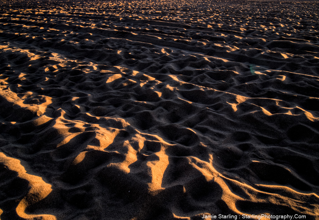 A beautiful sunset casting warm light and long shadows over the rippled sand, illustrating the natural beauty of imperfections and inviting reflection.