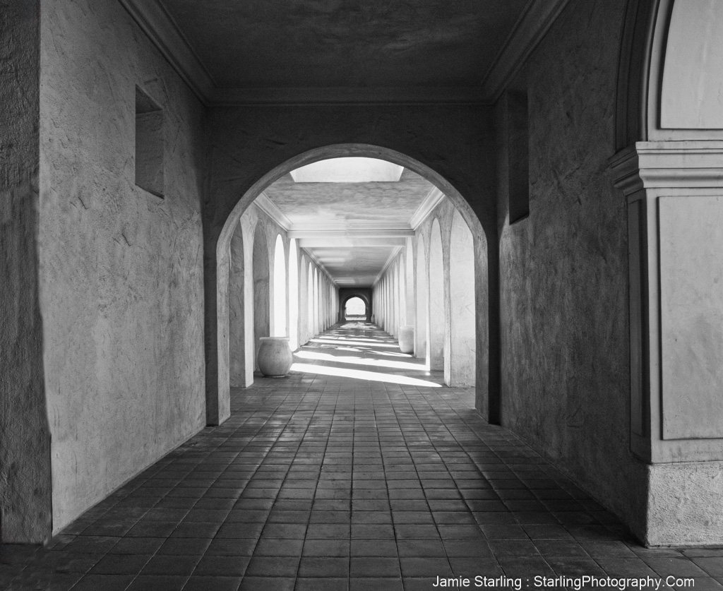 A serene and contemplative black and white image of an arch-lined corridor, where patterns of light and shadow evoke thoughts on the dual nature of life's journey.