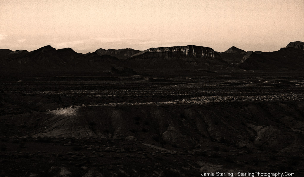 A tranquil black and white photograph of a sweeping desert landscape, with distant mountains under a broad sky, symbolizing the peace and vastness that slow travel offers.