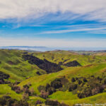 A captivating view of lush green hills beneath a wide, clear blue sky, embodying growth and the vast potential of life's journey, encouraging viewers to explore their own inner landscapes and hidden needs.