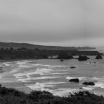 A peaceful black and white coastal landscape with gentle waves, misty horizons, and rocky shorelines, symbolizing life's rhythms, challenges, and resilience, compelling viewers to explore their inner peace and strength.