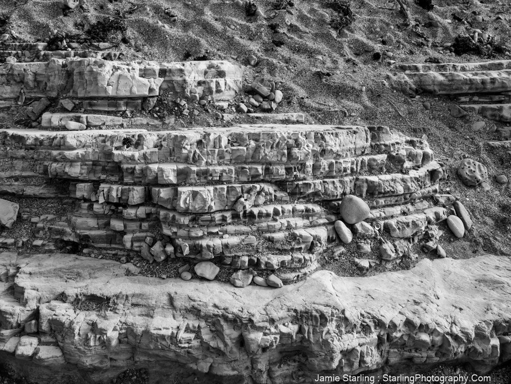 Black-and-white photo of layered rock formations, inviting contemplation on life's journey and the transformations that add depth and wisdom.