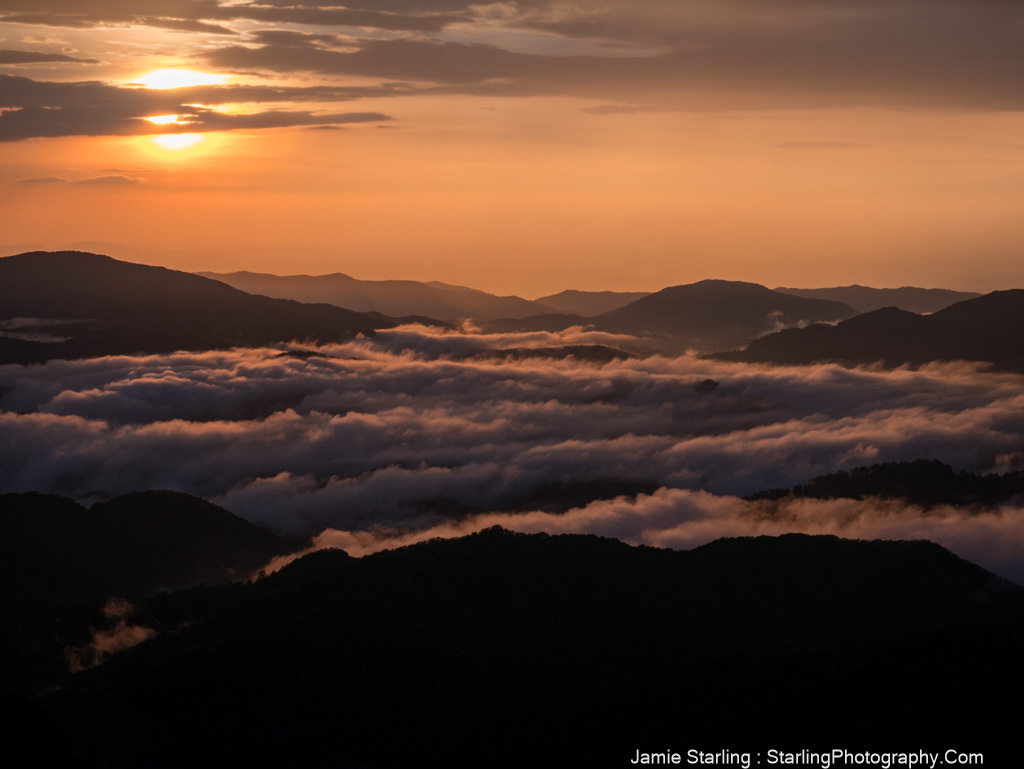 A peaceful sunset over mountains and clouds, bathed in soft golden light, showcasing nature's tranquil beauty.