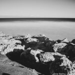 A serene black and white photo of a rocky shoreline with gentle waves, illustrating the harmony of self-acceptance and personal growth, inviting viewers to explore deeper life lessons.
