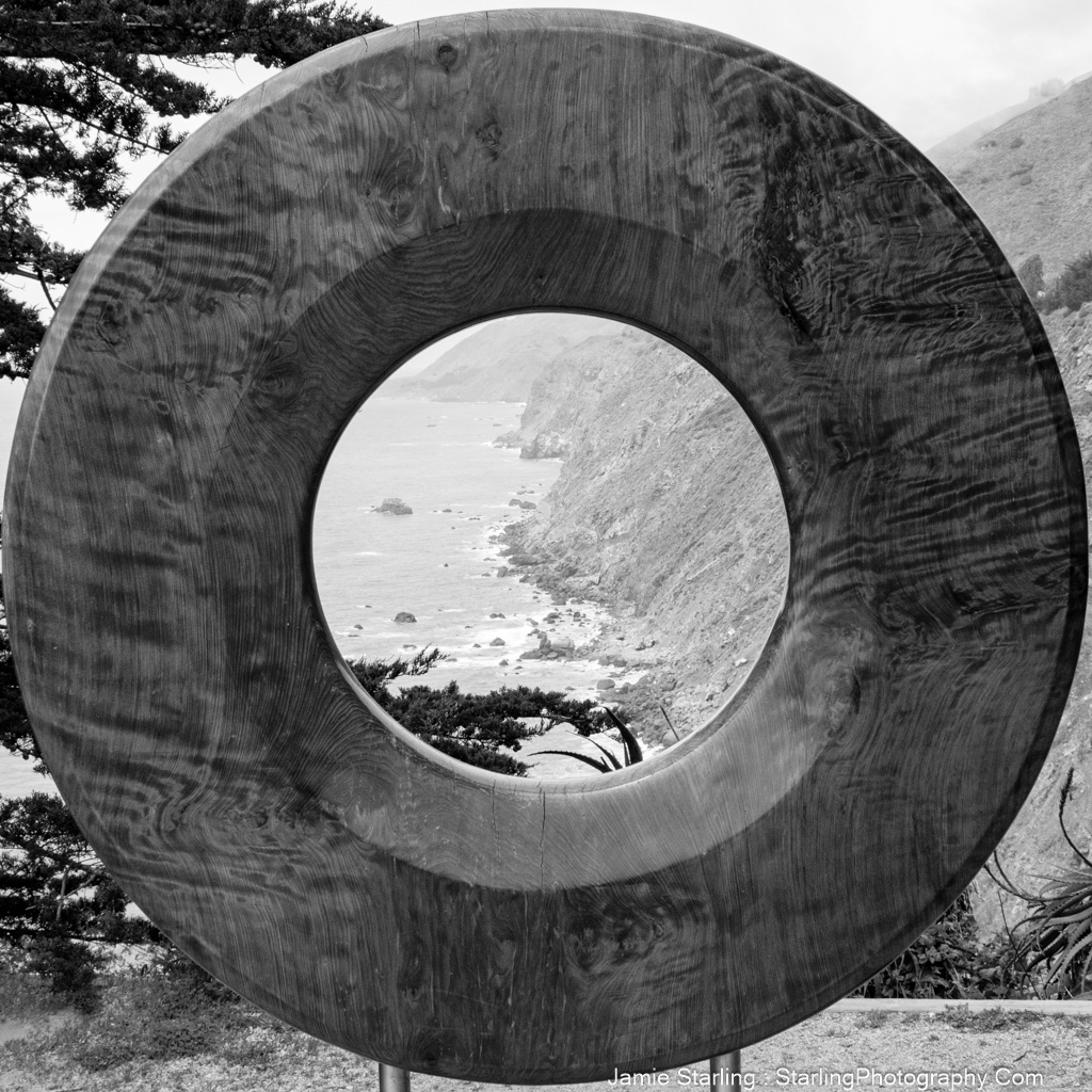 A black and white photo of a circular wooden sculpture framing a distant ocean view, representing the journey of self-discovery and finding authenticity beyond societal influences.