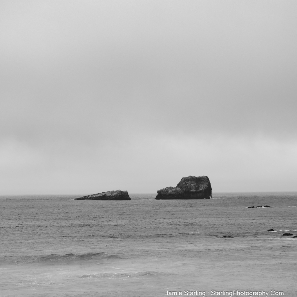 A serene black and white photo of two rocks in the ocean, representing the idea of balancing compassion with empowerment to avoid fostering dependency.