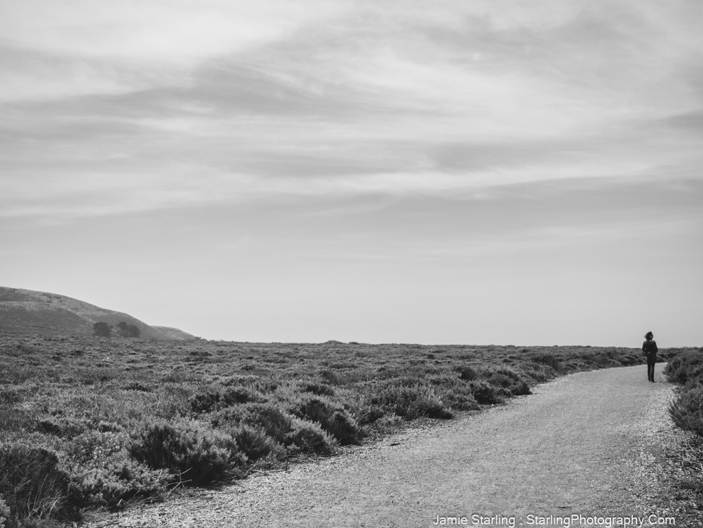 A black and white image of a person walking alone on a quiet path through a vast, peaceful landscape, symbolizing self-discovery and inner peace.