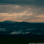 Evening light breaking through misty mountains, symbolizing the beginning of awakening and the clarity that follows.