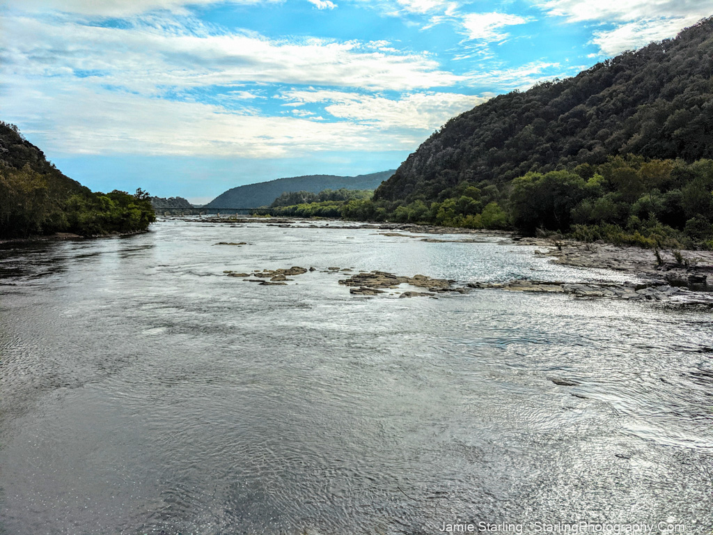 A calm river flows between green hills under a partly cloudy sky, symbolizing the harmony between going with the flow and taking necessary actions in life.