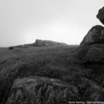 Black and white image of solid rocks and misty fields, symbolizing the importance of grounding in the present moment for inner peace and spiritual connection.