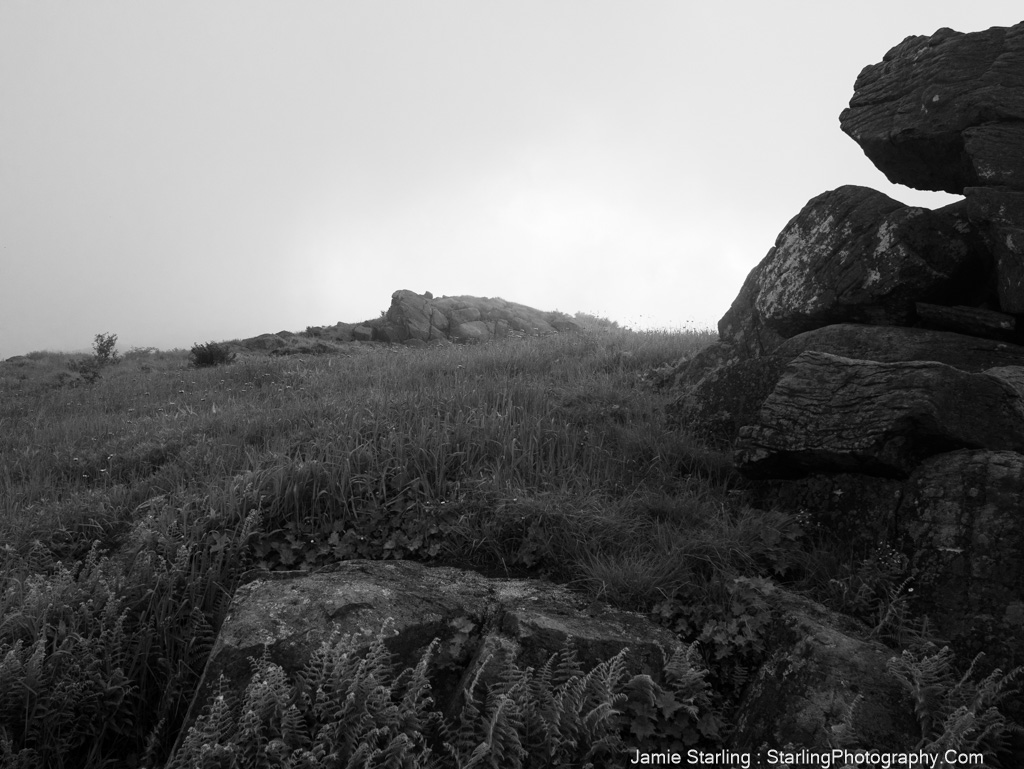 Black and white image of solid rocks and misty fields, symbolizing the importance of grounding in the present moment for inner peace and spiritual connection.