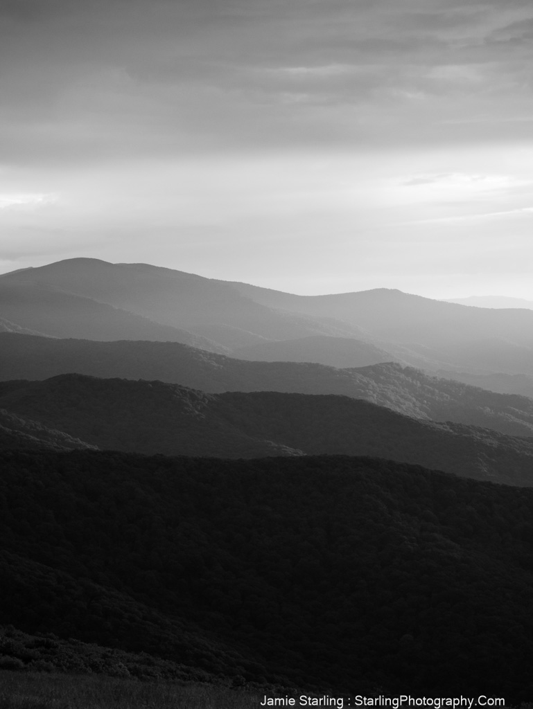 Black-and-white photograph of layered mountain ridges with light breaking through clouds, symbolizing the power of perspective and the depth of life's layers.