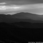 Darkened mountain ranges with light breaking through clouds, symbolizing the journey from belief in external authority to discovering the power within.