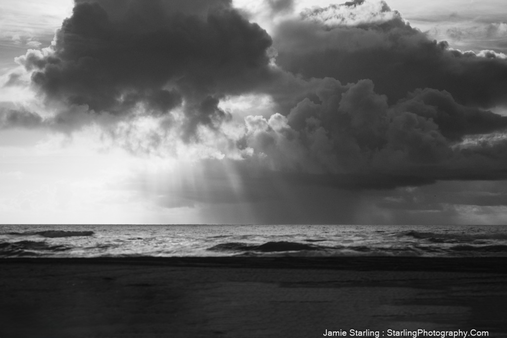 Dark clouds over the ocean with rays of light breaking through, symbolizing moments of clarity piercing through illusions.