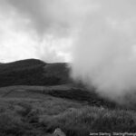 A black-and-white image of rolling hills with drifting clouds, symbolizing the balance between clarity and uncertainty in life’s journey, evoking a sense of reflection and connection.