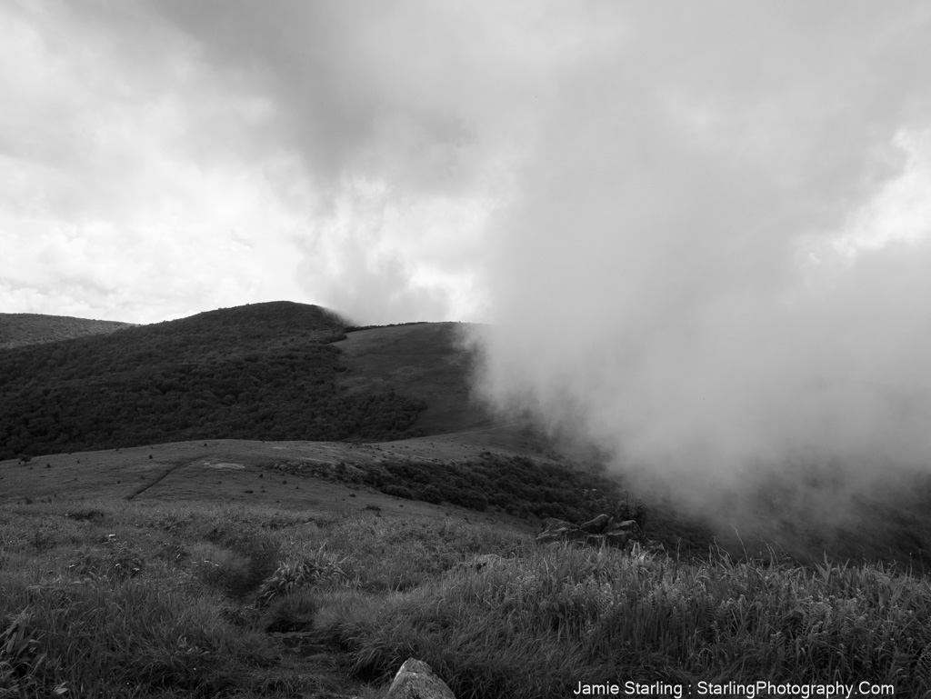 A black-and-white image of rolling hills with drifting clouds, symbolizing the balance between clarity and uncertainty in life's journey, evoking a sense of reflection and connection.