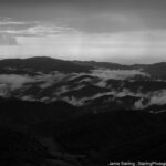 Black-and-white image of misty mountains with light breaking through, symbolizing the revealing power of truth and the illusions that cloud our perception.