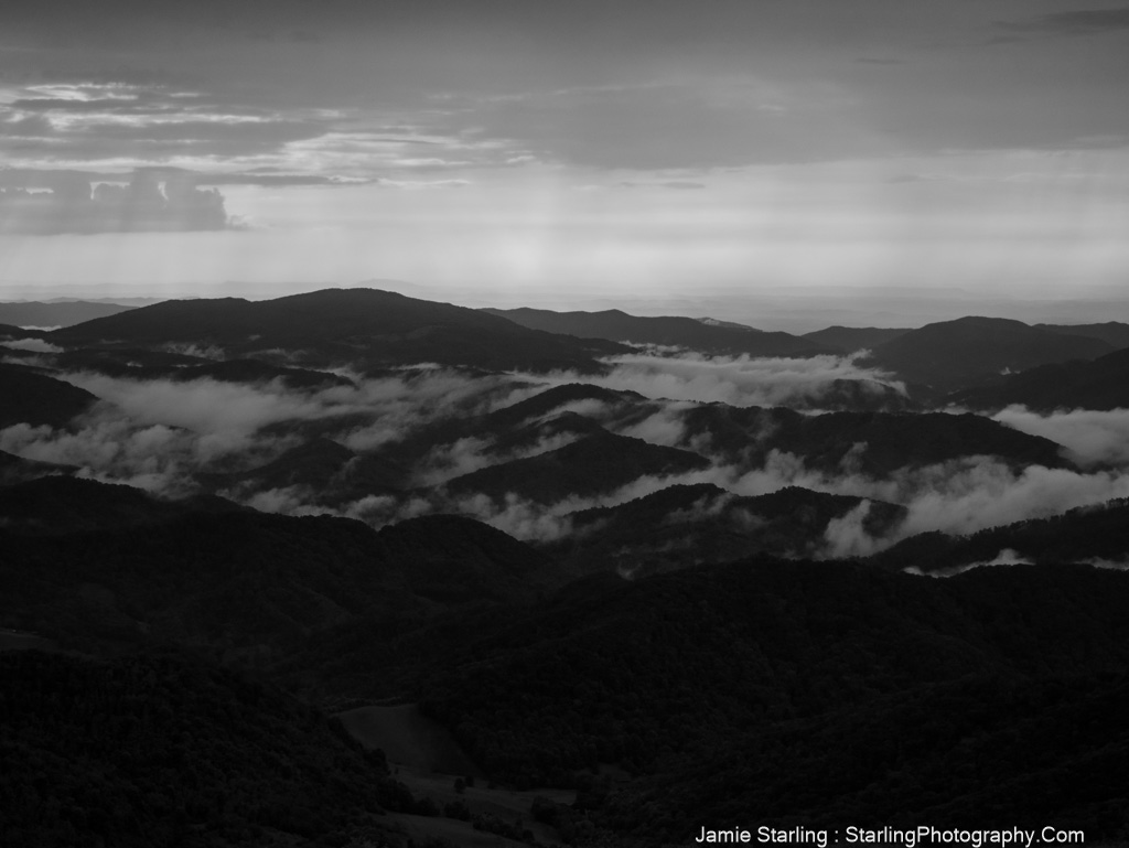 Black-and-white image of misty mountains with light breaking through, symbolizing the revealing power of truth and the illusions that cloud our perception.