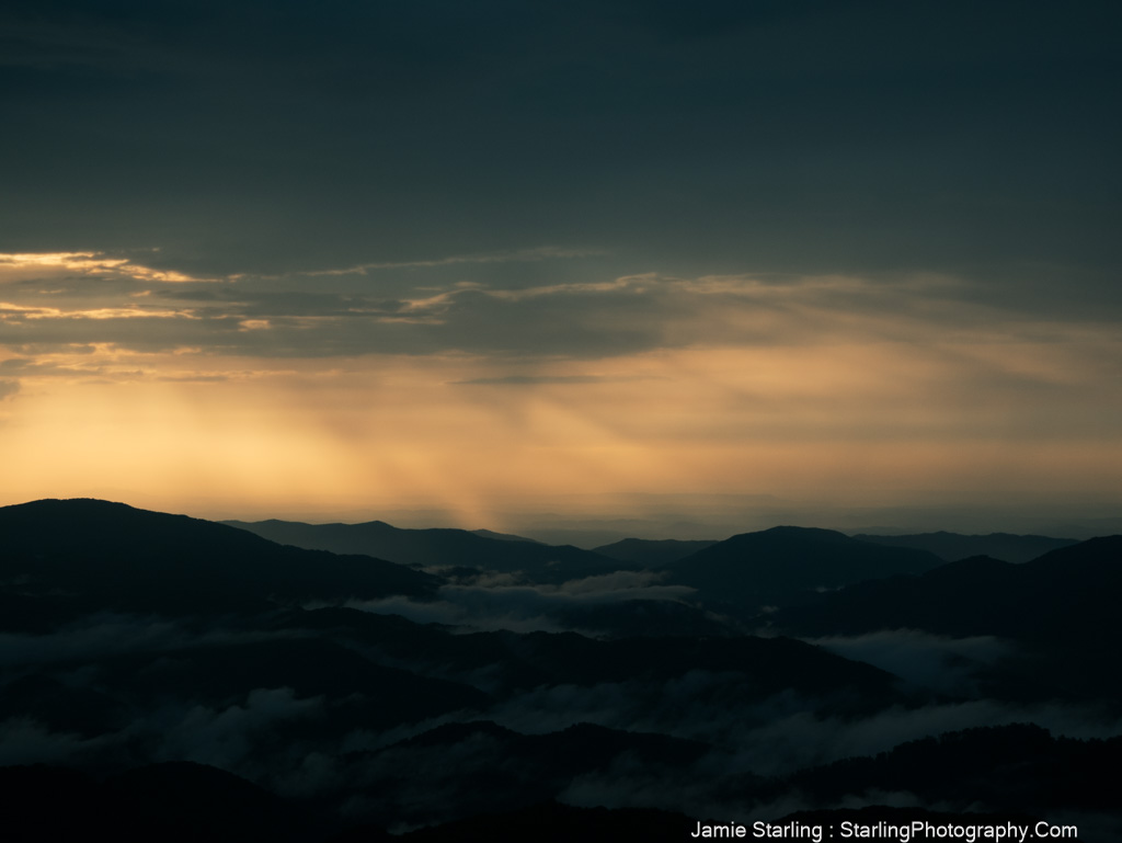 Sunlight breaking through clouds over misty mountain ridges, symbolizing the journey from blindness to insight and uncovering hidden truths.