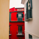 Vivid red building surrounded by tight neutral-colored walls with a narrow space in between, symbolizing breaking free from societal constructs.