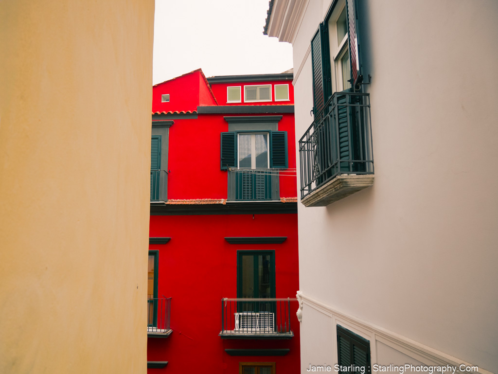 Vivid red building surrounded by tight neutral-colored walls with a narrow space in between, symbolizing breaking free from societal constructs.