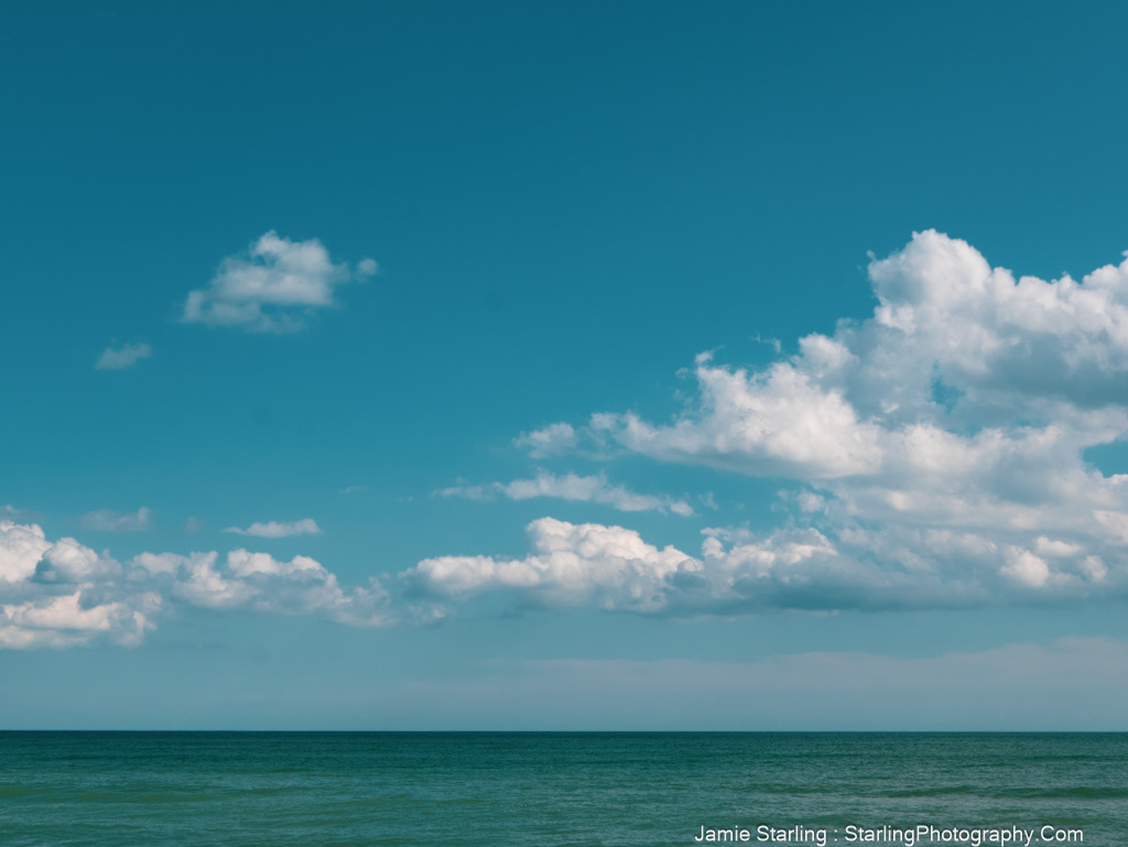 A peaceful ocean meets a bright blue sky with drifting clouds, symbolizing the tension between illusion and reality, freedom and security.