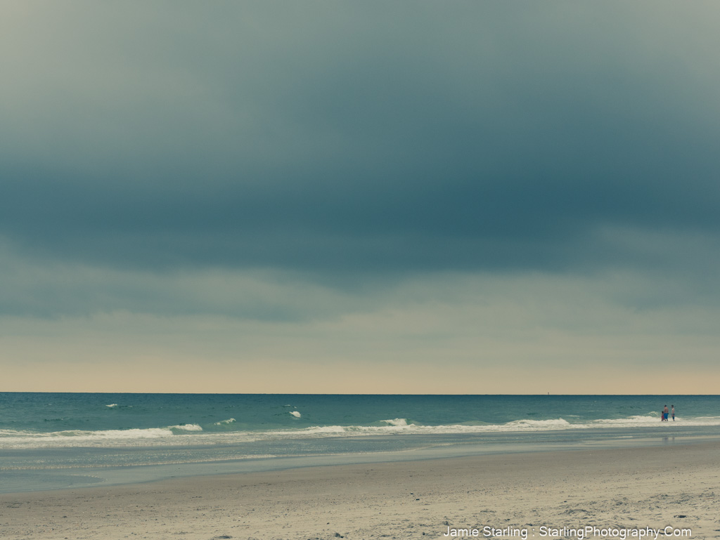 A couple walking along a quiet beach under a cloudy sky, symbolizing the power of showing up in the present moment, even amidst uncertainty.