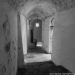 A quiet alleyway in black and white with soft light from a single lantern, highlighting rough-textured walls and shadows, inviting the viewer to pause and reflect on the beauty of simple spaces.