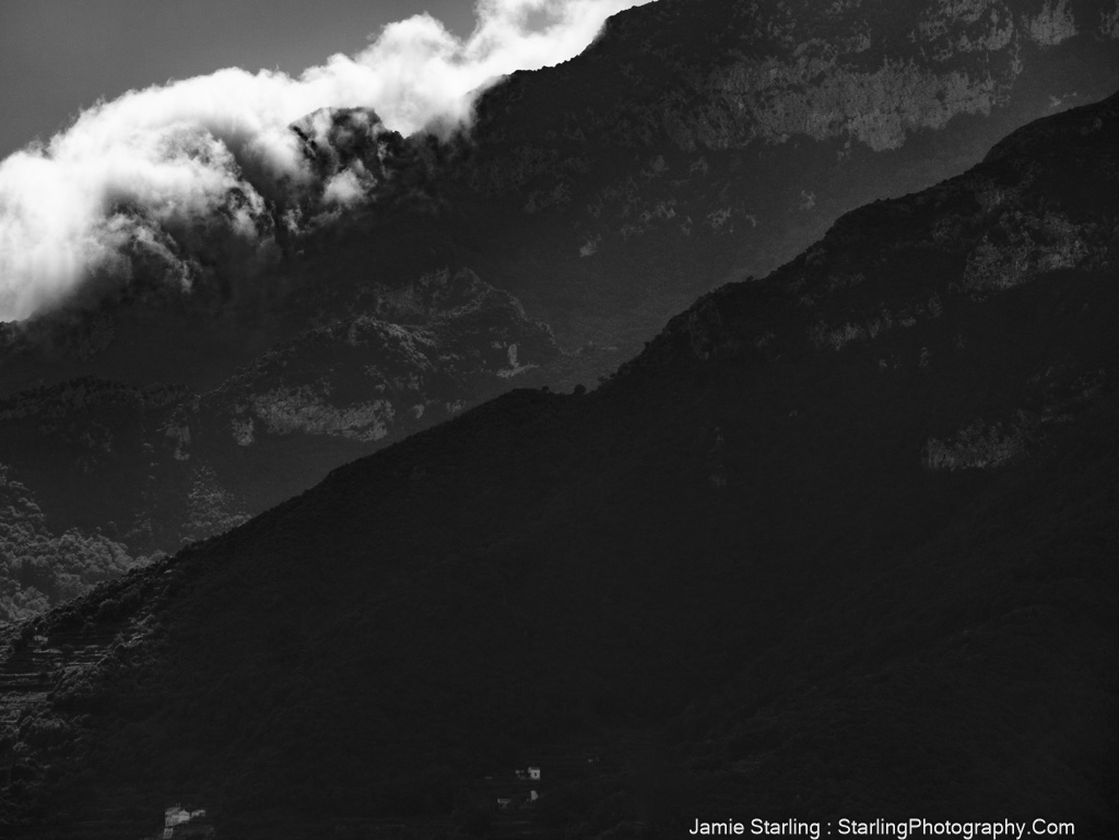 A black-and-white photo of rugged mountains with light breaking through mist, creating a dramatic contrast between light and shadow.